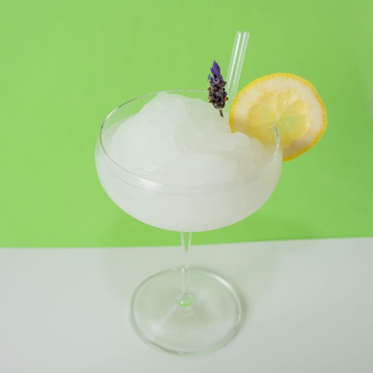 Cóctel de daiquiri de limón congelado servido en vaso, decorado con rodaja de limón y hielo triturado.