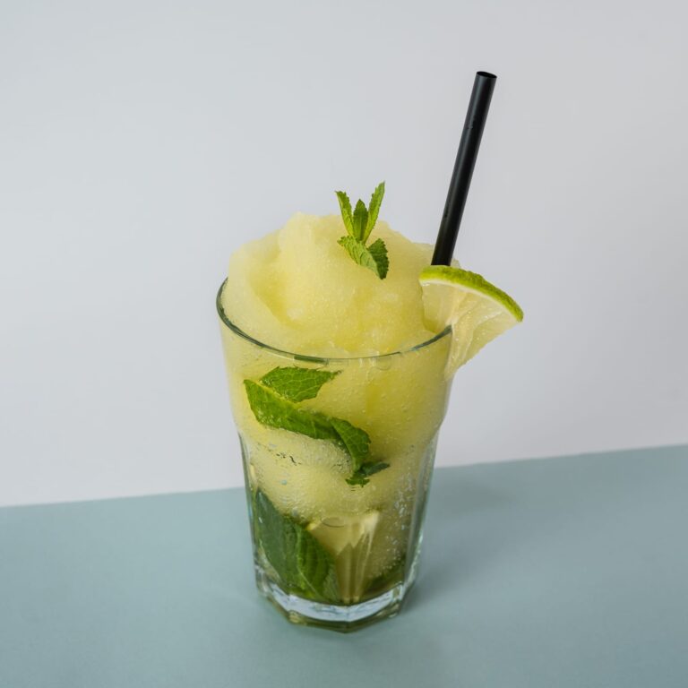 Cóctel de mojito congelado servido en vaso con hierbabuena fresca, rodaja de lima y hielo triturado