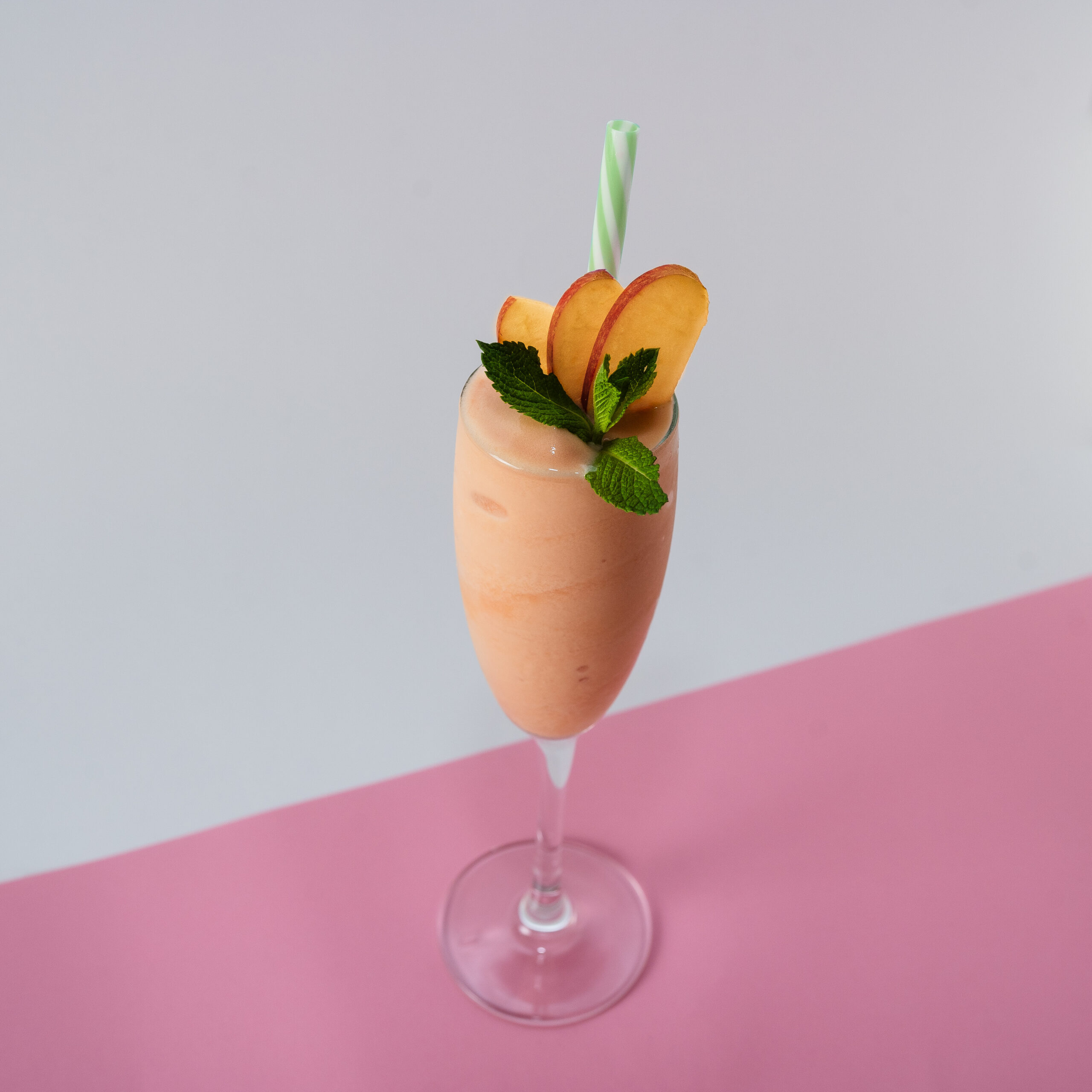 Un refrescante Frozen Bellini servido en una copa de champán, con un delicado tono melocotón y una textura escarchada, decorado con una rodaja de durazno y una ramita de menta.