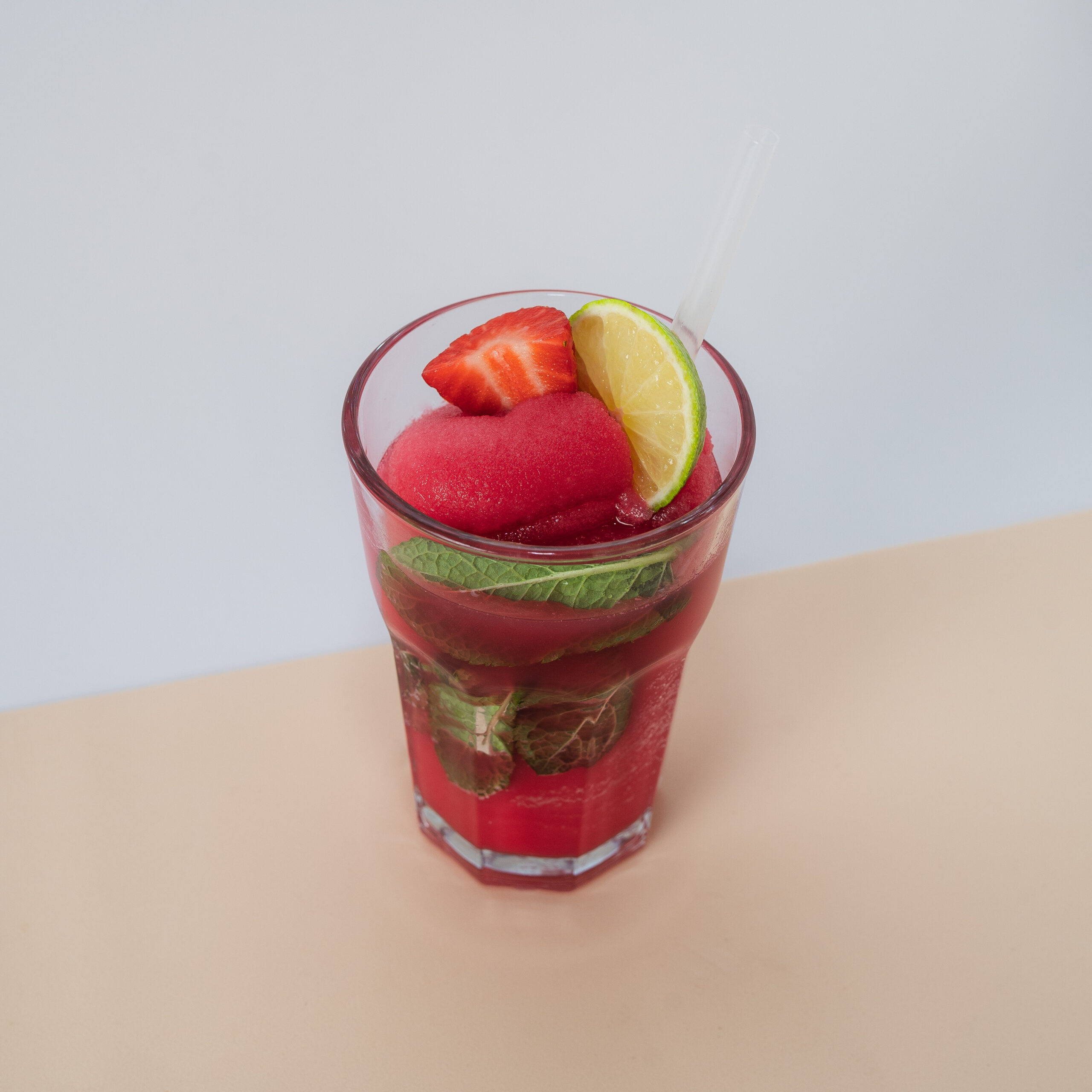 Un vibrante Frozen Mojito de Fresa servido en un vaso alto, con un intenso color rojo y una textura helada, decorado con rodajas de lima, fresas frescas y hojas de menta.